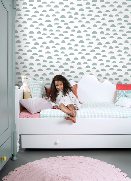 Kinderzimmer mit Mädchen auf einem Bett, Tapete mit Halbkreis Muster, Kleiderschrank und Teppich