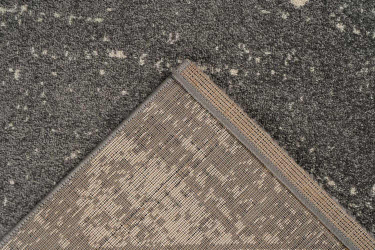 Nahaufnahme eines grauen Teppichs mit gesprenkeltem Muster, die die gekettelte Kante und die strukturierte Rückseite zeigt.