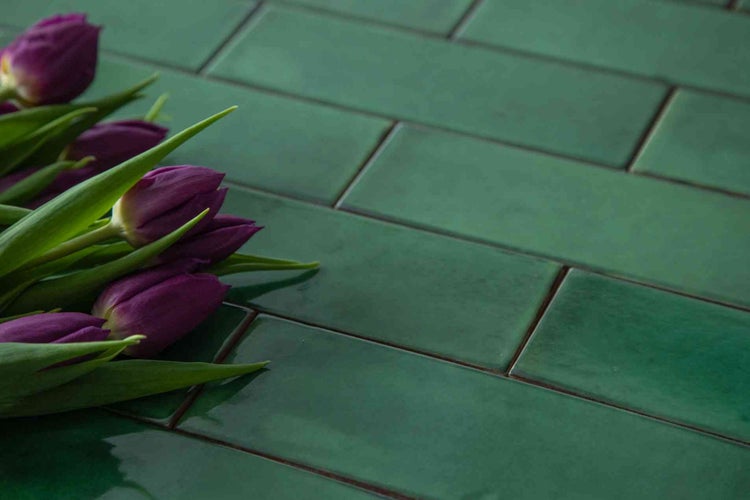 Grüne glänzende Wandfliesen im Metro-Stil in Ziegeloptik mit lila Tulpen.