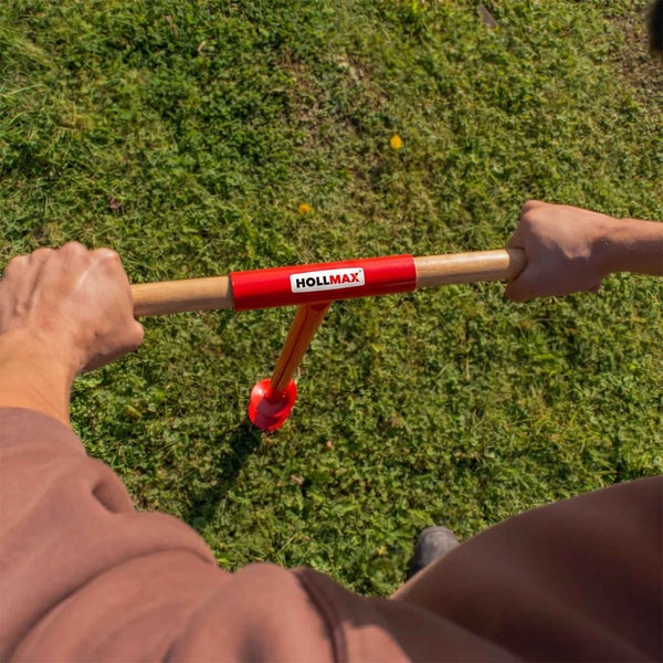 Eine Person benutzt einen manuellen Erdbohrer mit Holzgriff und Hollmax Logo, um Löcher in einen Rasen zu bohren.