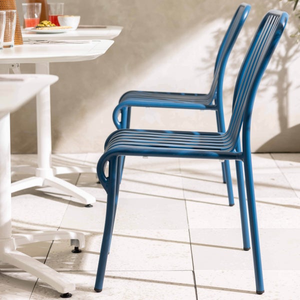 Blaue Gartenstühle aus Metall im Bistro-Stil an einem weißen Gartentisch auf einer hellen Terrasse.