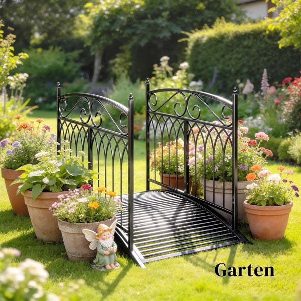 Dekorative Gartenbrücke aus schwarzem Metall auf einer Rasenfläche, umgeben von Blumentöpfen aus Terrakotta und einer kleinen Gartenfigur.