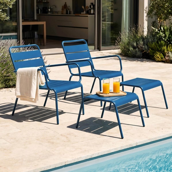Modernes Gartenmöbel-Set aus blauem Metall mit zwei Sesseln und zwei Hockern auf einer sonnigen Terrasse am Pool.