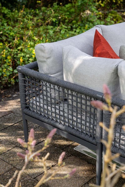 Nahaufnahme eines Gartensofas mit Seilgeflecht, grauen Kissen und Metallgestell auf einer Terrasse.