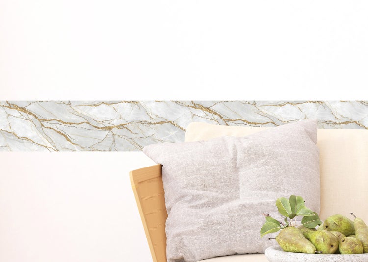 Tapetenbordüre mit Marmor-Optik und goldfarbenen Adern an einer Wand über einem Sofa mit Kissen und einer Schale Birnen.