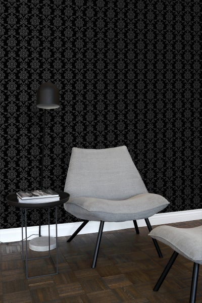 Raumansicht mit schwarzer Vliestapete mit Ornamentmuster, Sessel und Stehleuchte.