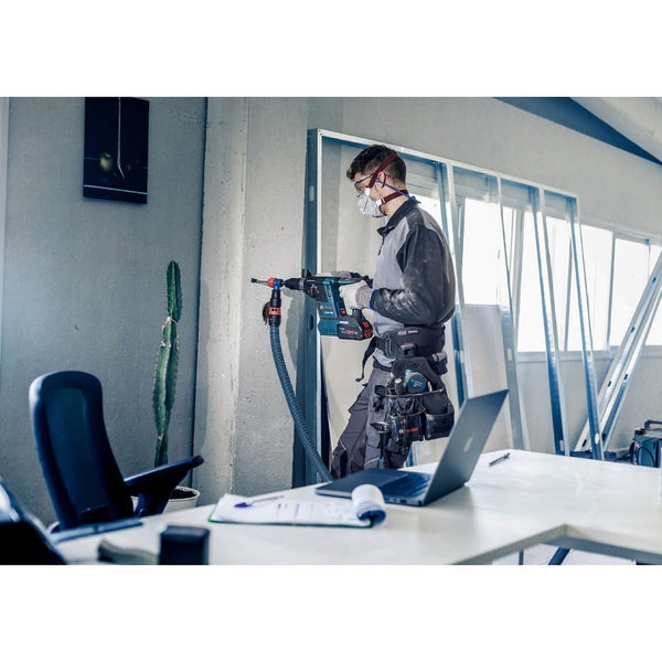 Handwerker bohrt mit einem Bohrhammer in eine Wand, Staubabsaugung ist angeschlossen.