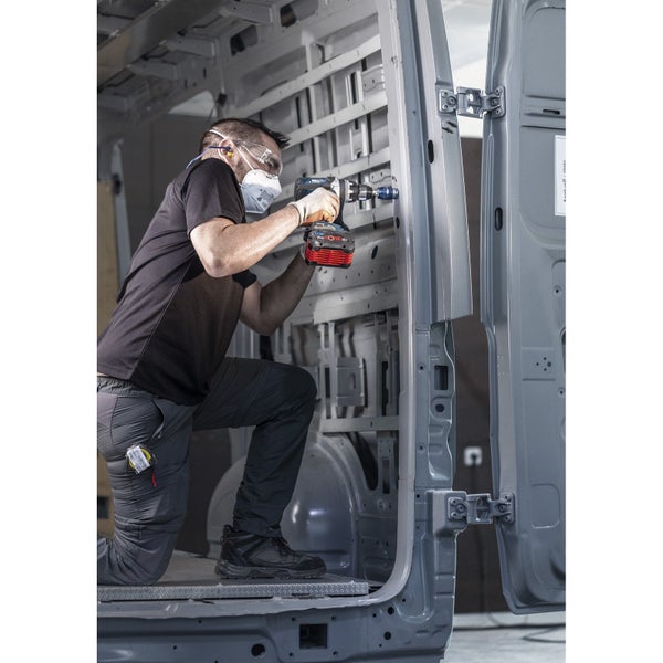 Handwerker arbeitet mit einer Bohrmaschine in einem Lieferwagen, mit Schutzkleidung ausgestattet.