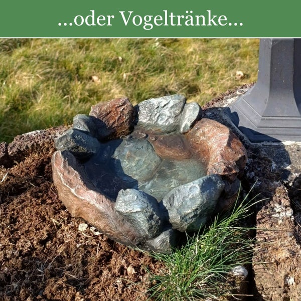 Vogeltränke in Steinoptik im Garten auf Erde platziert.