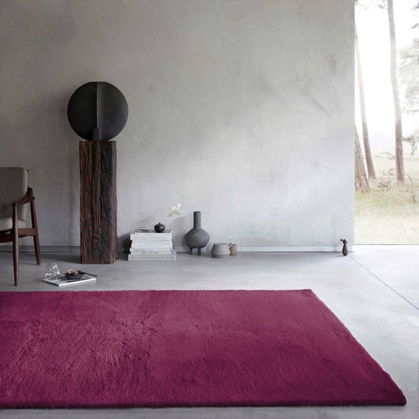 Rechteckiger Hochflor-Teppich in einem minimalistischen, hellen Wohnzimmer mit Betonboden, strukturierter Wand und dekorativen Objekten.