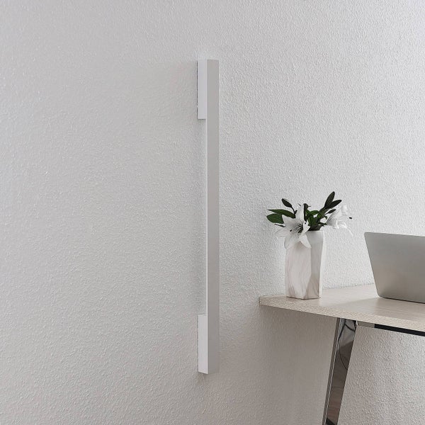 Moderne vertikale LED-Wandleuchte an strukturierter Wand neben einem Schreibtisch mit Blumen und Laptop in hellem, modernem Ambiente.