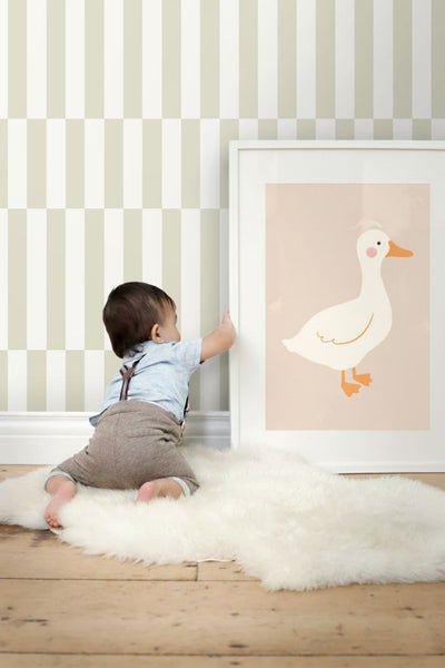 Beige und weiß gestreifte Tapete in einem hellen Kinderzimmer mit einem Kind auf einem Fellteppich vor einem gerahmten Wandbild.