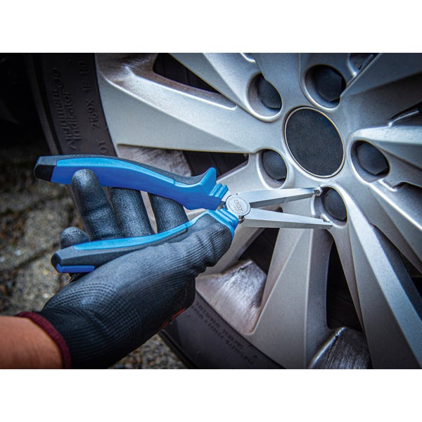 Eine Hand mit Schutzhandschuh benutzt eine Spitzzange an einer Felge.