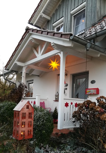 Weihnachtlich geschmückter Hauseingang mit einem leuchtenden Herrnhuter Stern unter dem Vordach und einem beleuchteten Metallhaus als Dekoration.
