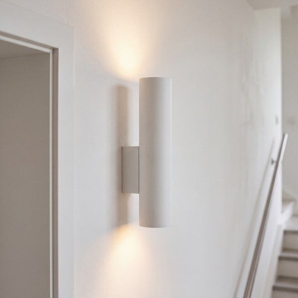 Moderne zylindrische Wandleuchte mit Lichtaustritt nach oben und unten an einer hellen Treppenhauswand.