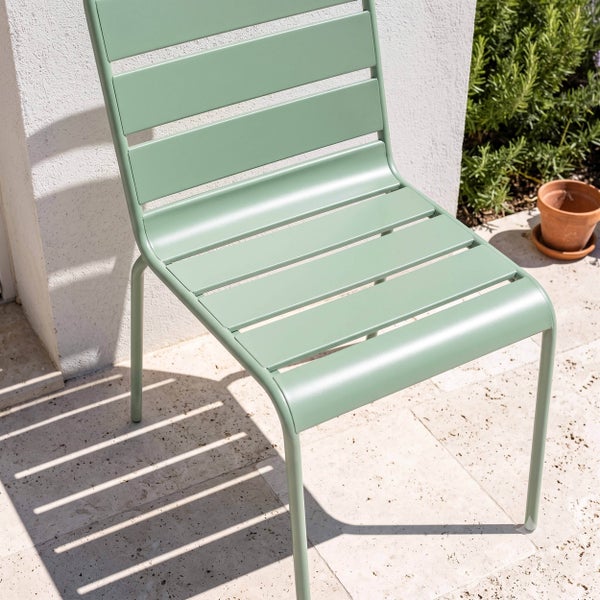 Grüner Gartenstuhl aus Metall mit Latten-Design auf einer hellen, sonnigen Steinterrasse.