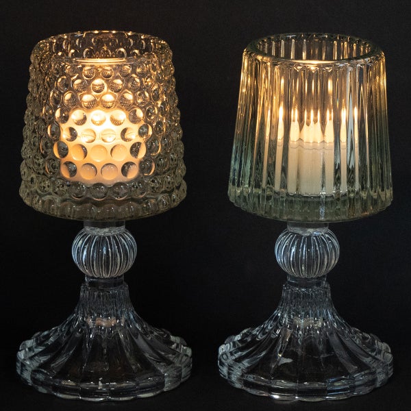 Dekorative Anordnung mit einer Keramikvase, Trockenblumen und zwei gläsernen Teelichthaltern mit brennenden Kerzen auf einer Holzoberfläche.