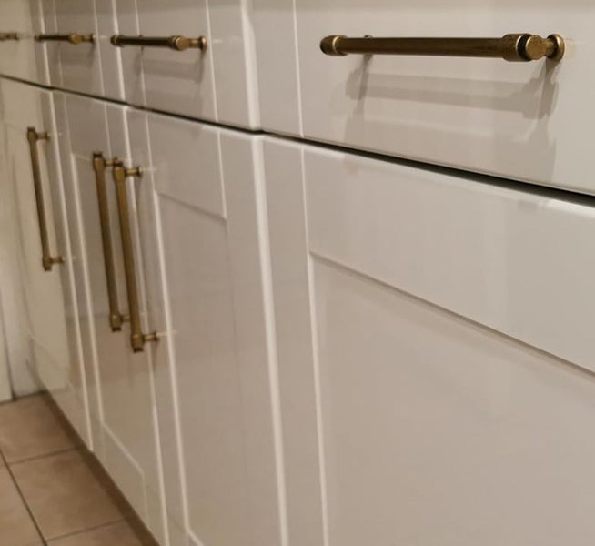 Moderne weiße Küchenschränke mit Kassettenfronten und horizontalen sowie vertikalen Möbelgriffen aus Metall in Messingoptik.