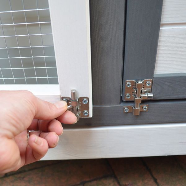 Nahaufnahme einer Hand, die einen Metall-Schieberiegel an einer Holztür eines Kleintierstalls mit Drahtgeflecht bedient.