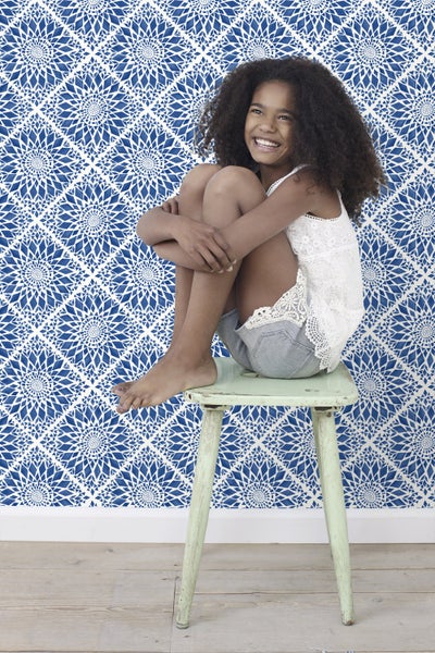Mädchen sitzt auf einem Hocker vor einer Wand mit geometrischer Tapete