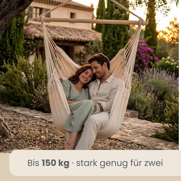 Ein Paar sitzt in einem cremefarbenen Hängesessel mit Holzstab in einem mediterranen Garten. Belastbar bis 150 Kilogramm.