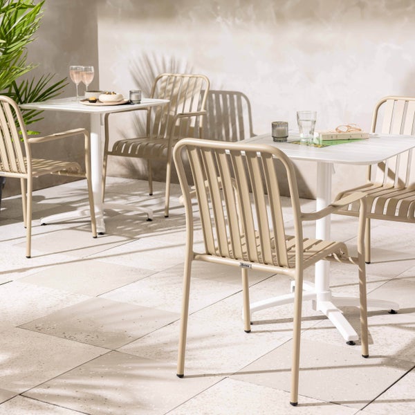 Modernes Gartenmöbel-Set mit weißen quadratischen Bistrotischen und beigen Metallstühlen mit Lattenoptik auf einer hellen Fliesenterrasse.
