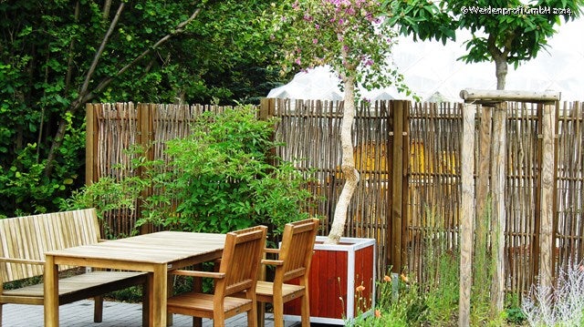 Gartenbereich mit Holzzaun, Gartentisch und Stühlen.
