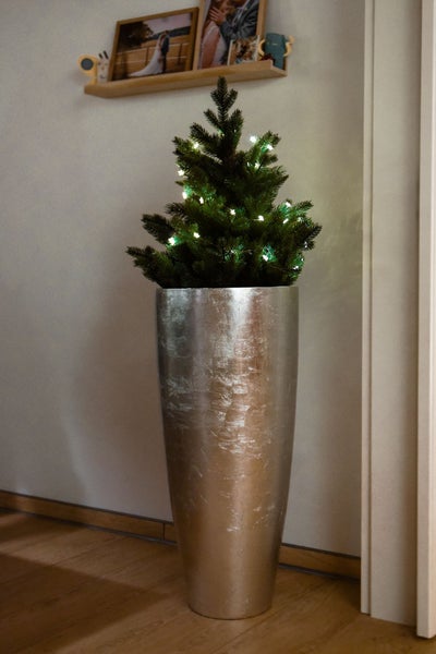 Kleiner künstlicher Weihnachtsbaum mit LED-Beleuchtung in einer hohen silbernen Bodenvase mit strukturierter Oberfläche.