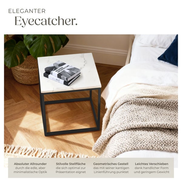 Quadratischer Beistelltisch mit Marmoroptik-Platte und schwarzem Metallgestell in einem Schlafzimmer neben einem Bett auf Parkettboden.