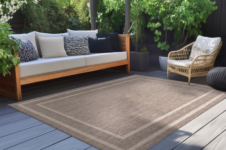 Rechteckiger Outdoor Teppich mit strukturierter Oberfläche und Bordüre auf einer Holzterrasse mit Lounge Möbeln.