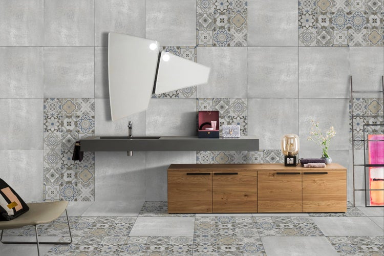 Helles Badezimmer mit grauen und gemusterten Fliesen, Waschtisch, Spiegel und Holzkommode.