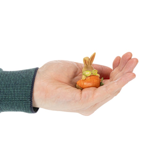 Kleine dekorative Hasenfigur mit Karotte und Brille in einer Hand zum Größenvergleich.