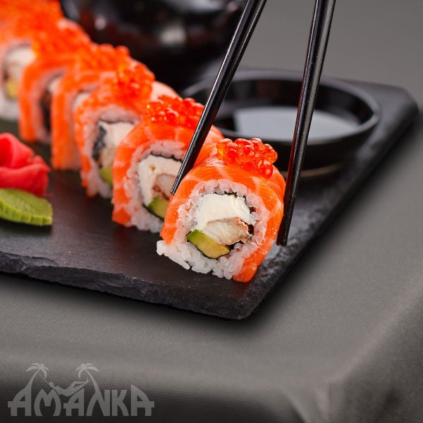 Sushi-Rolle mit Lachs, Frischkäse, Avocado und Fischrogen auf einem Teller, gehalten von Essstäbchen