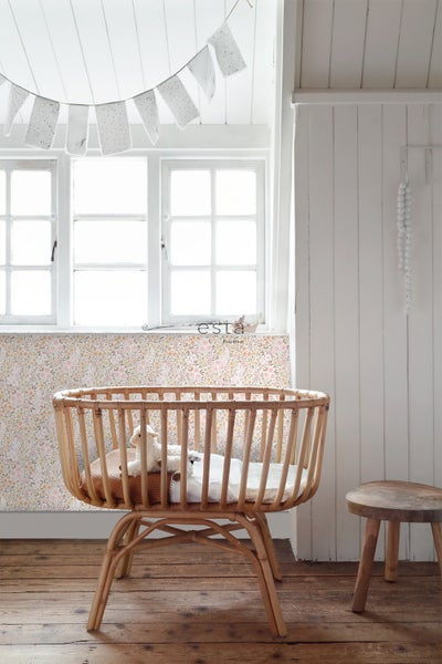 Babyzimmer mit einem Kinderbett aus Rattan, einer Fensterdekoration und einer hölzernen Hocker