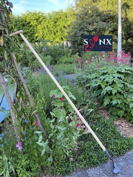 Gartenhacke mit Holzstiel vor Gartenkulisse