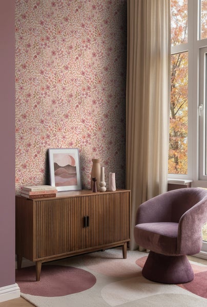 Helles Zimmer mit geblümter Tapete, einem Sideboard aus Holz mit Dekorationsartikeln, einem lila Sessel und einem Fenster mit Vorhängen.