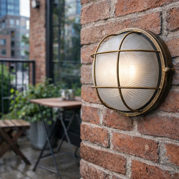 Runde Außenwandleuchte mit Metallgitter und geriffeltem Glas montiert an einer Ziegelwand im Außenbereich.