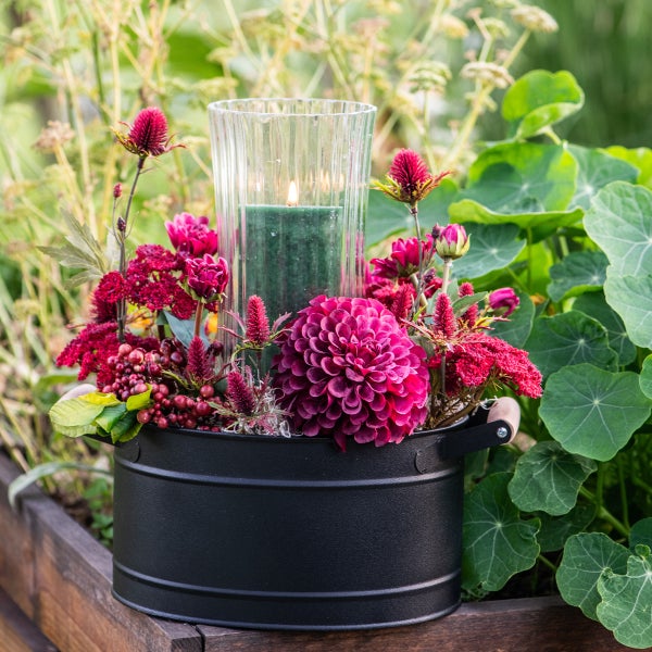 Dekorative Blumengesteck mit Kerze in schwarzem Eimer