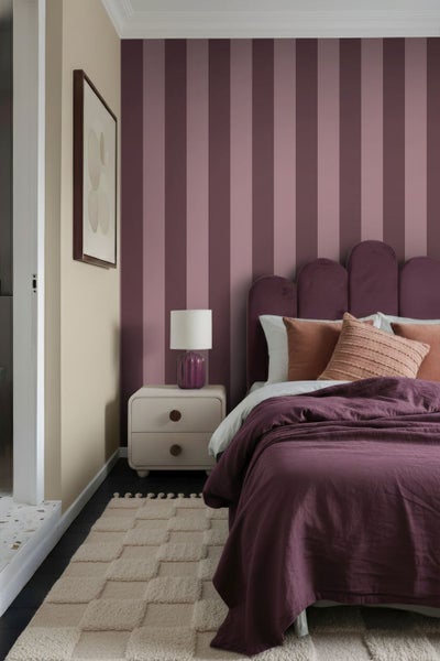 Modernes Schlafzimmer mit gestreifter lila Akzentwand, gepolstertem Bett mit lila Bettwäsche, weißem Nachttisch und einem strukturierten beigen Teppich.