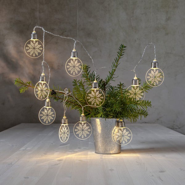 Dekorative Lichterkette mit Schneeflockenmotiv in einem Topf mit Tannenzweigen auf einem Tisch