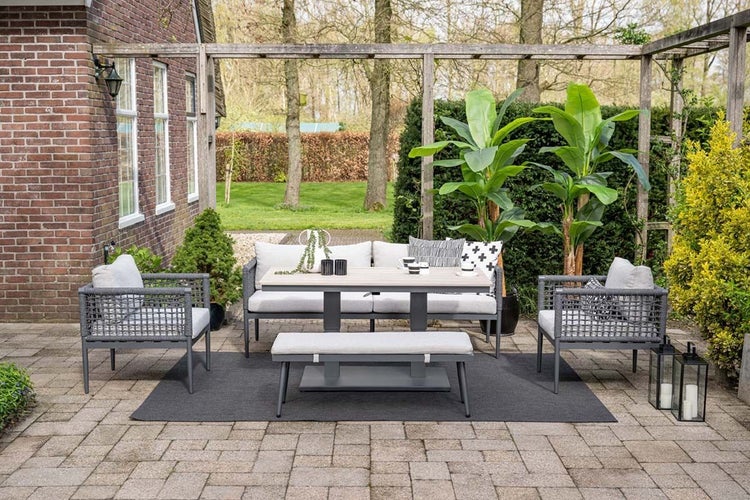 Modernes Garten Lounge Set aus Seilgeflecht mit Sofa, Sesseln, Bank, Tisch und Polstern auf einer gepflasterten Terrasse im Garten.