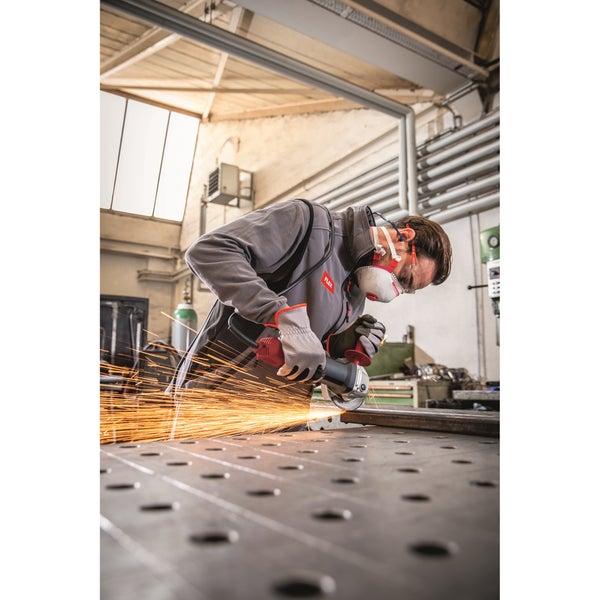 Handwerker mit Schutzausrüstung bei der Arbeit mit einem Winkelschleifer an einem Werkstück in einer Werkstatt.
