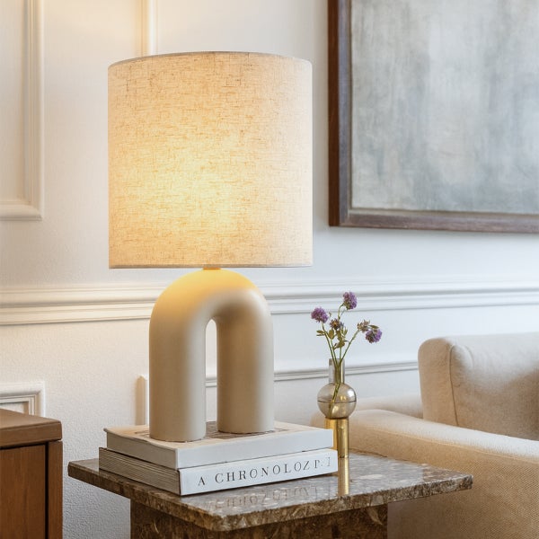 Tischleuchte mit beigem Lampenschirm und U-förmigem Sockel auf Büchern