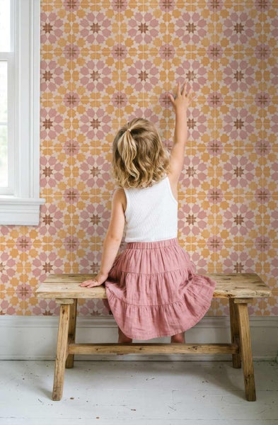Tapete mit geometrischem Sternenmuster an einer Wand, die von einem Kind auf einer Holzbank berührt wird, in einem hellen Raum.