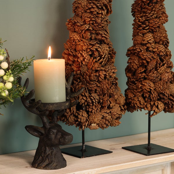 Dekorative Szene mit Kerze in Hirschkopf-Kerzenständer und Tannenzapfen-Weihnachtsbäumen