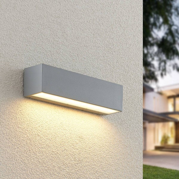 Moderne rechteckige LED-Außenwandleuchte in Silber, an einer strukturierten Fassade montiert, mit warmweißem Lichtschein nach unten.