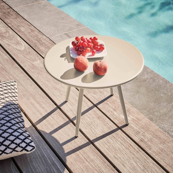 Runder Beistelltisch aus Metall in Beige auf einer Holzterrasse am Pool mit Trauben und Pfirsichen.