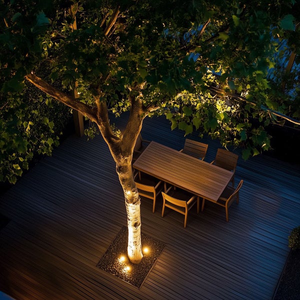 Beleuchtete Holzterrasse bei Nacht mit einem Baum, einem rechteckigen Holztisch und Gartenstühlen aus Holz in stimmungsvoller Atmosphäre.