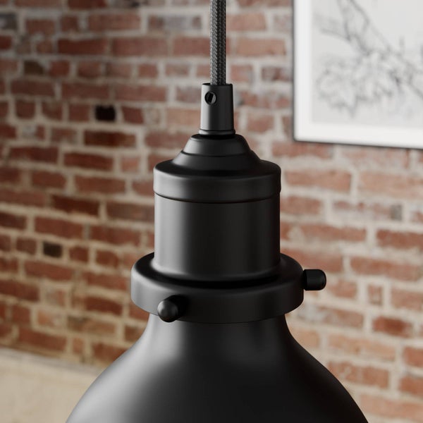 Nahaufnahme einer schwarzen Pendelleuchte mit Textilkabel und Lampenfassung im Industrie-Design vor einer Ziegelwand.