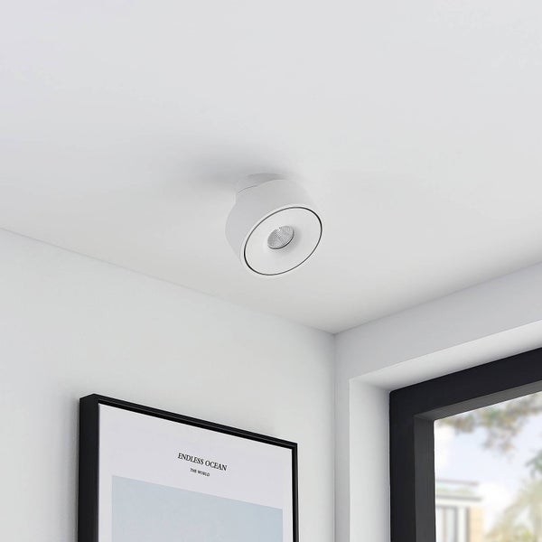 Zylindrische, weiße Deckenleuchte als Spot, montiert an einer weißen Decke in einem modern gestalteten Wohnraum.